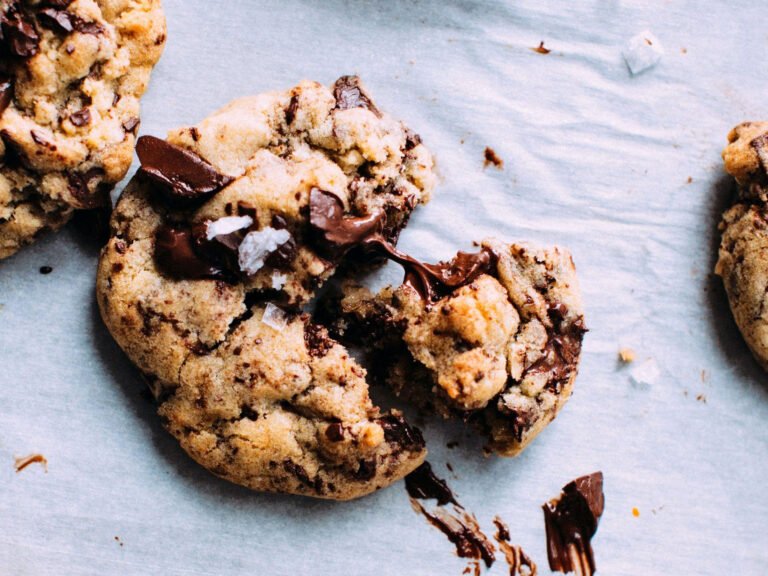 Chocolate chip cookies with melted chocolate and sea salt on parchment paper, highlighting a broken cookie for texture and freshness.