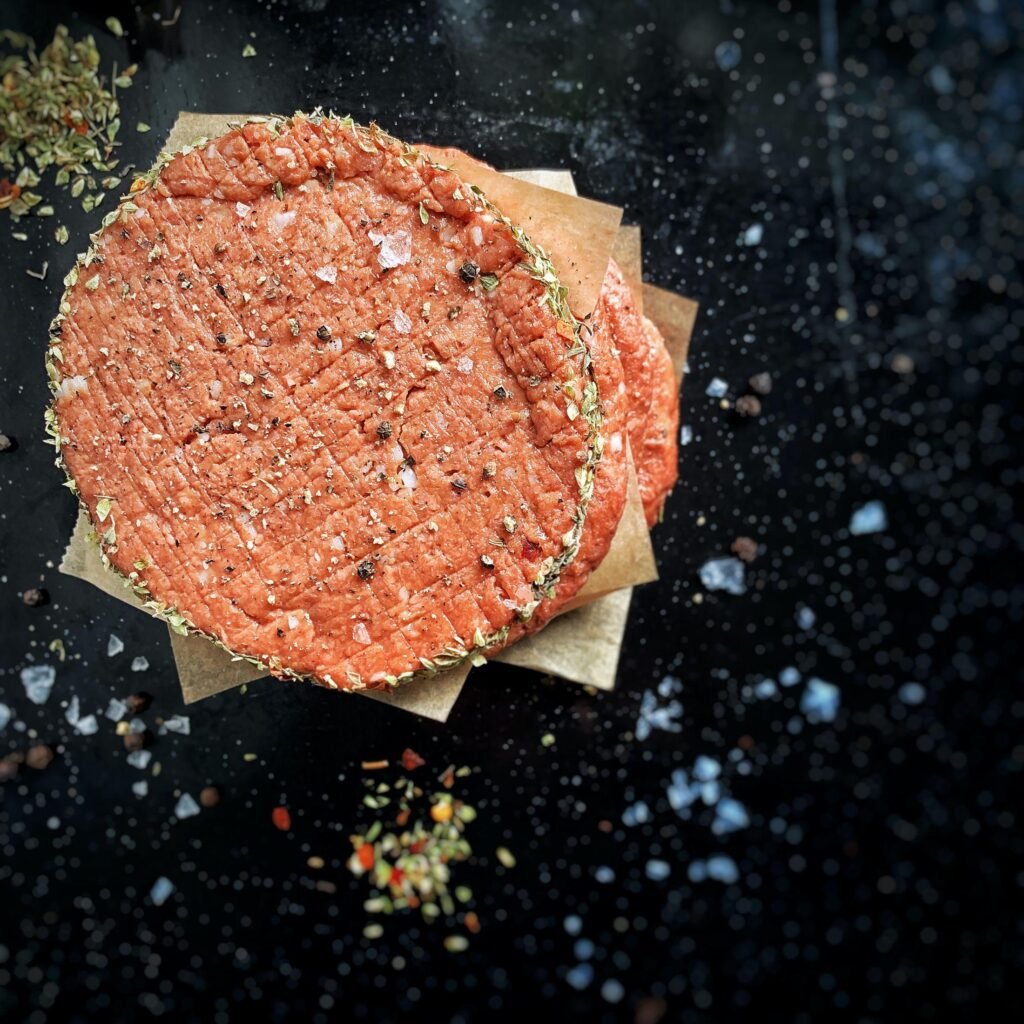 Smoky Chipotle burger patties stacked on parchment paper, garnished with herbs and spices, against a dark backdrop.