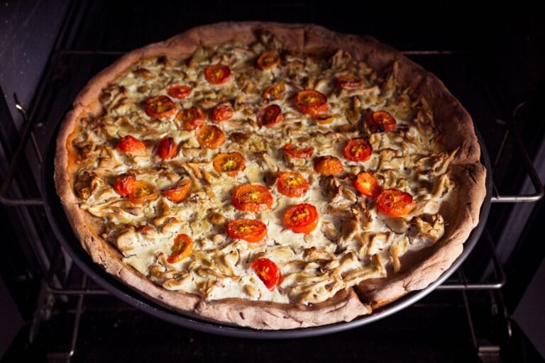 Pizza with cherry tomatoes and chicken, baking in the oven, highlighting a golden crust and fresh ingredients.