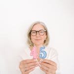 A senior woman holding number candles for a 45th birthday celebration.