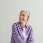 Charming senior woman in a purple shirt sits smiling indoors.