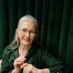 Elegant senior woman with eyeglasses smiling while holding a pen and reviewing documents indoors.