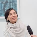 Middle-aged woman in interview setting with a microphone indoors.