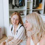 Two women smiling and bonding, seated in a modern wardrobe room, conveying positive emotions.